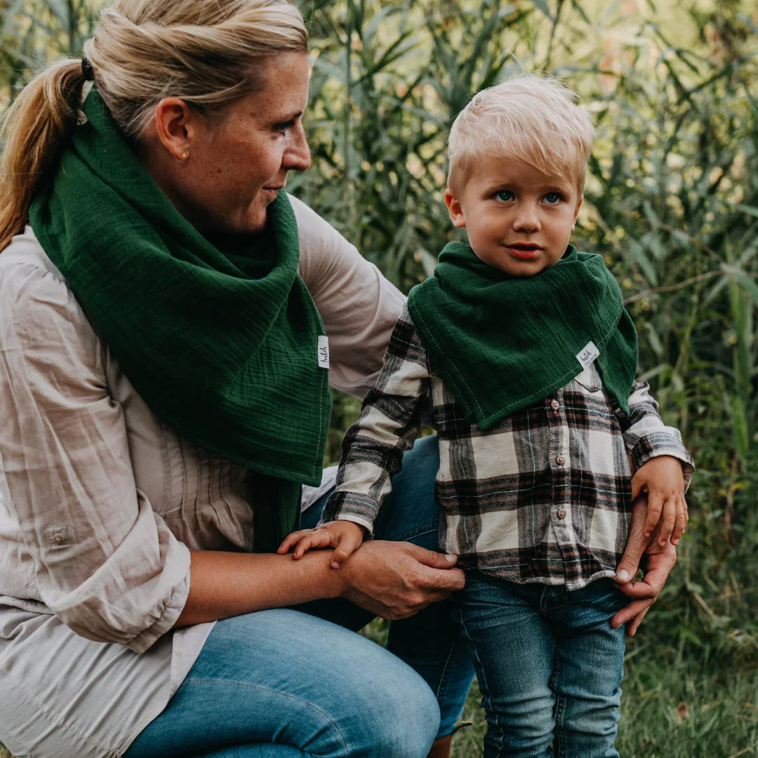 Eine Frau und ein kleiner Junge tragen beide grüne Musselin-Halstücher und stehen im Grünen; sie schauen sich liebevoll an.