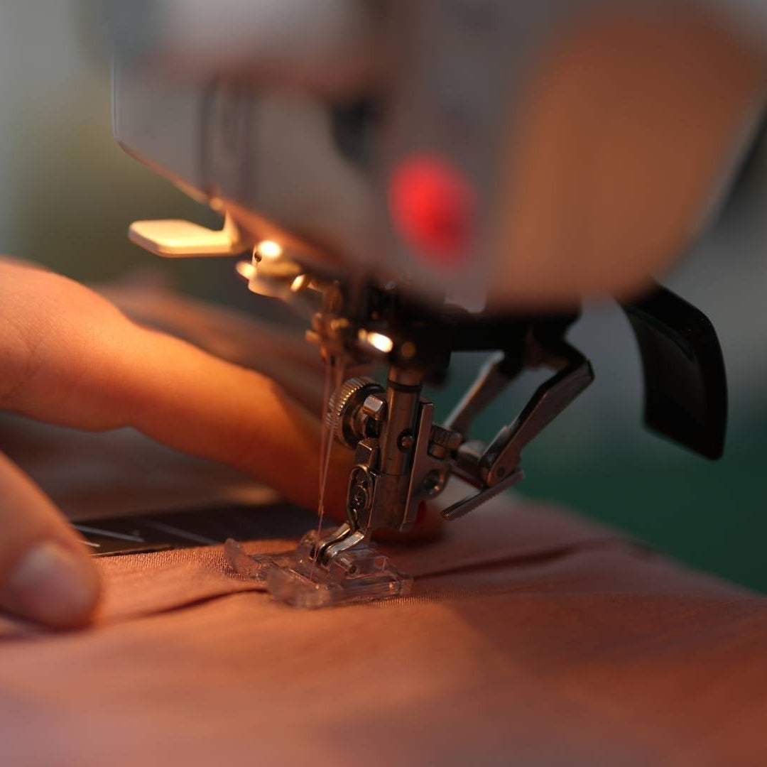 Hand führt Musselin Stoff unter einer Nähmaschine – detailreicher Blick auf das Nähen von Musselin mit feiner Nadel