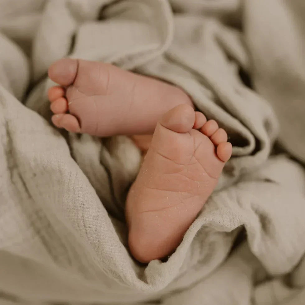 Babyfüße in weicher Musselin-Decke aus Bio-Baumwolle – zarte Strukturstoff-Falten, Symbol für Geborgenheit und Natürlichkeit