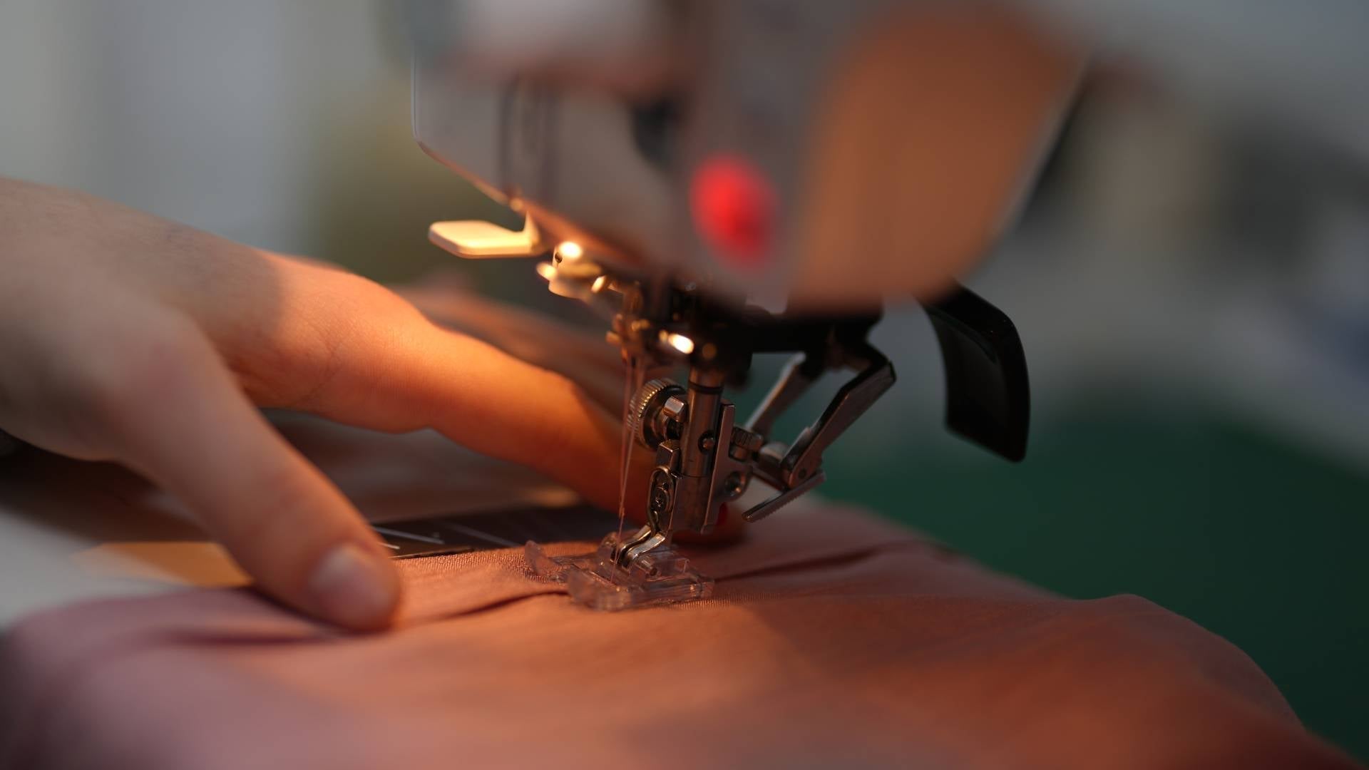 Hand führt Musselin Stoff unter einer Nähmaschine – detailreicher Blick auf das Nähen von Musselin mit feiner Nadel