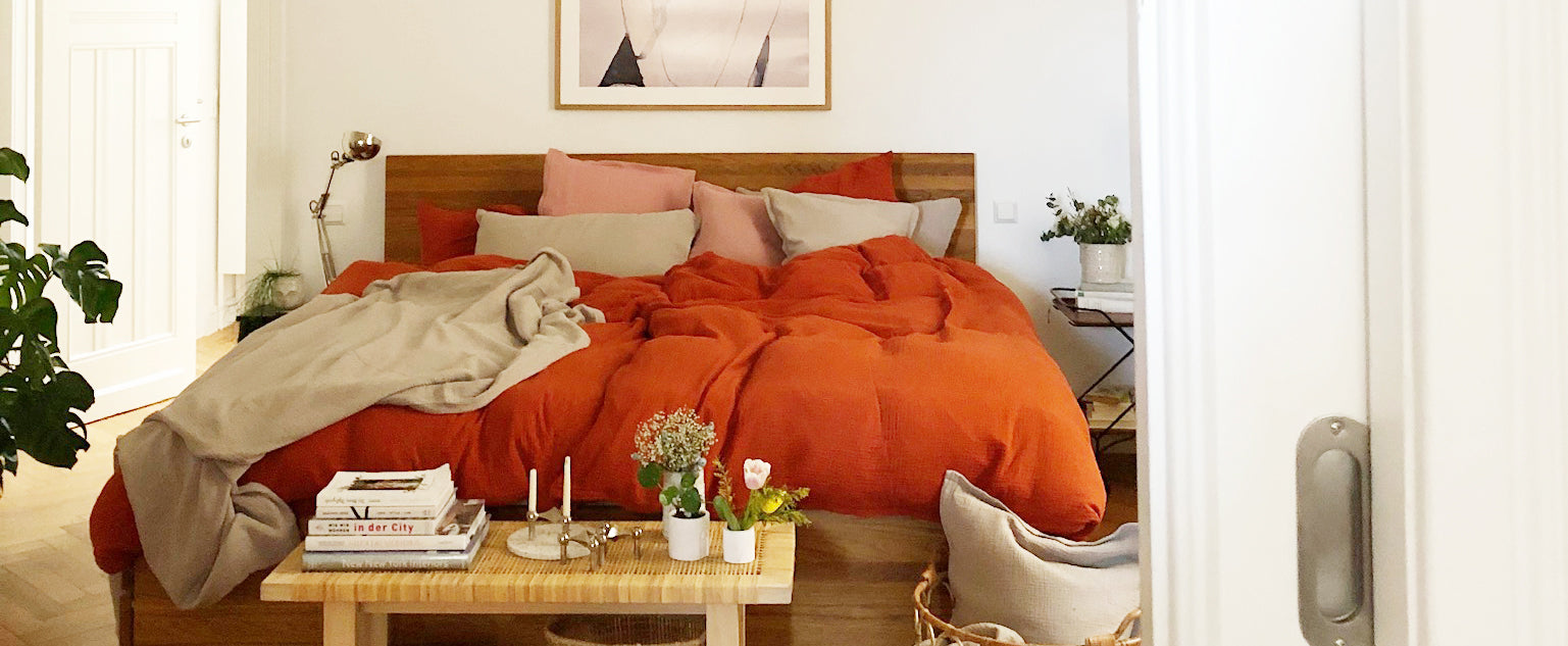 Schlafzimmer im Altbau mit modernen Holzbett und der eleganten Musselin-Bettwäsche von Hutch&Putch in Rostrot, kombiniert mit Kissen in Steingrau und Altrosa.